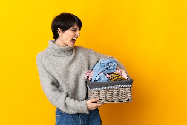 Mujer joven sosteniendo una canasta de ropa riendo en posición lateral