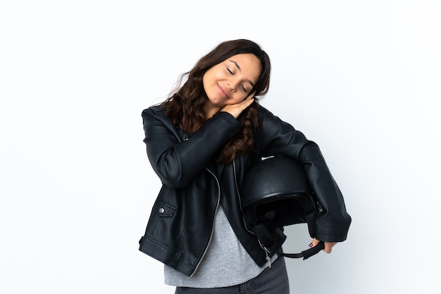 Mujer joven sosteniendo un casco de motocicleta sobre fondo blanco aislado haciendo gesto de sueño en expresión adorable