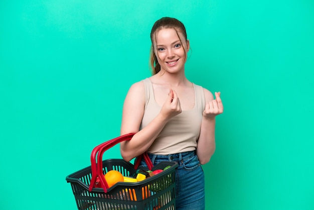 Foto mujer joven sosteniendo una cesta de la compra llena de alimentos aislado sobre fondo verde