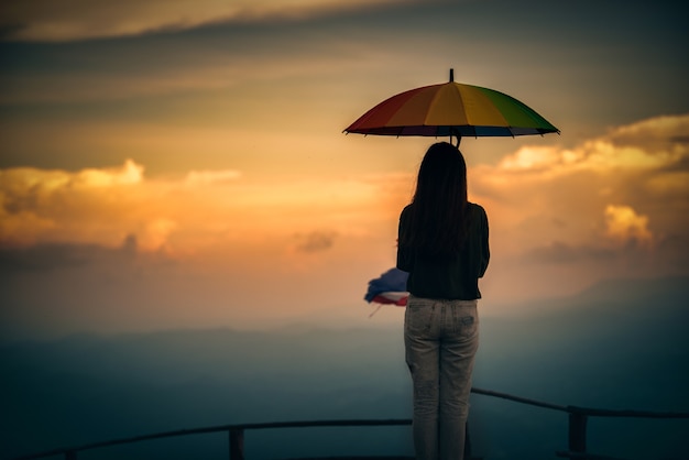 Mujer joven sosteniendo coloridos paraguas mirando lluvia en las montañas