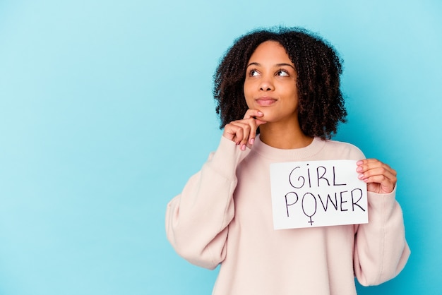 Mujer joven sosteniendo un concepto de poder femenino mirando hacia los lados con expresión dudosa y escéptica