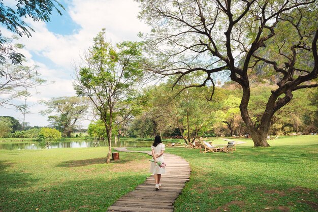 Mujer joven sosteniendo flores caminando por un sendero de madera en un jardín sombreado en un día brillante