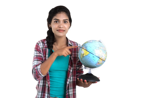 Mujer joven sosteniendo el globo terráqueo y posando sobre una pared blanca.