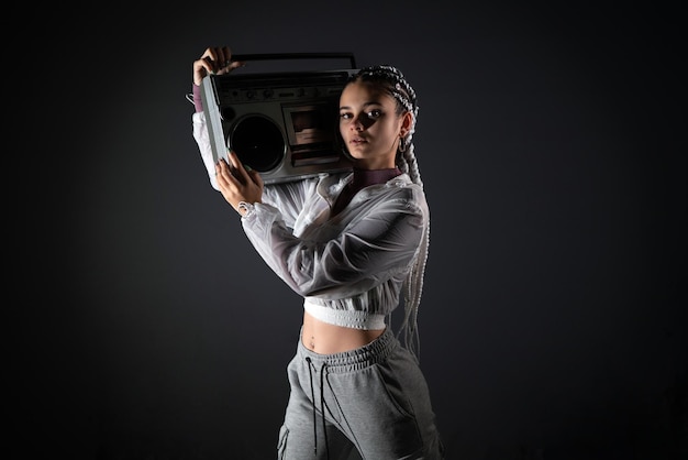 Mujer joven sosteniendo una grabadora retro en su hombro mientras mira a la cámara en una foto de estudio