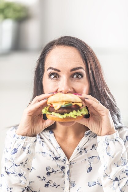 Mujer joven sosteniendo una hamburguesa frente a su boca.