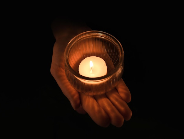 Mujer joven sosteniendo jar con vela encendida en la oscuridad