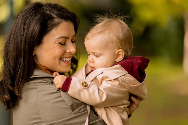 Foto mujer joven sosteniendo a una linda niña en el parque de otoño