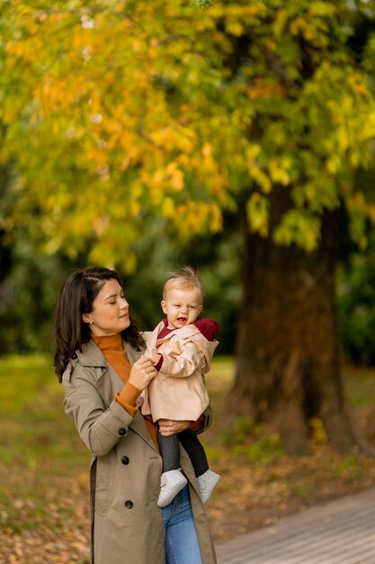 Foto mujer joven sosteniendo a una linda niña en el parque de otoño