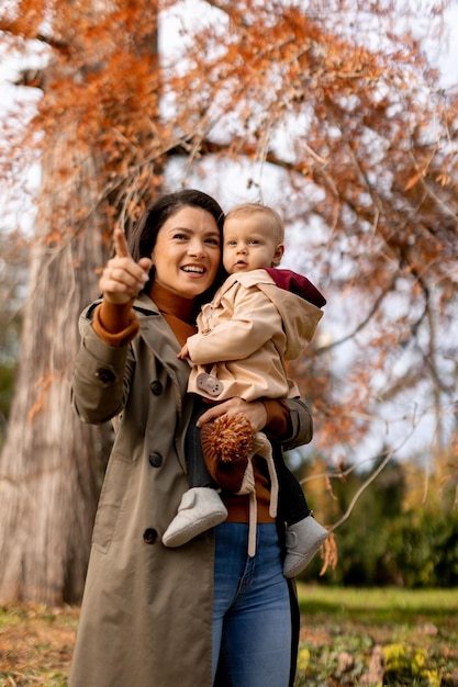 Foto mujer joven sosteniendo a una linda niña en el parque de otoño