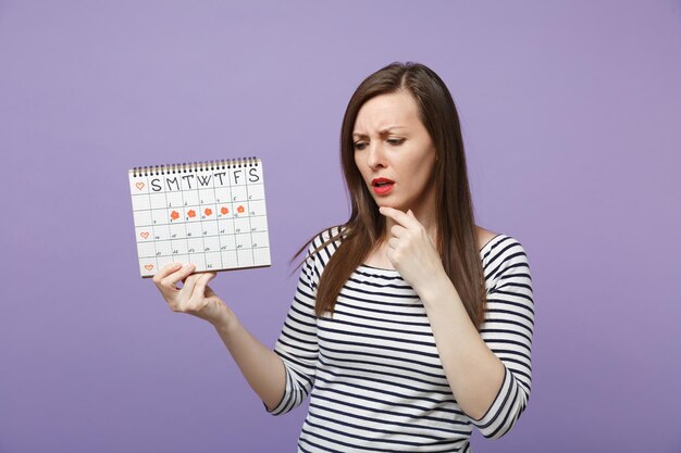 Mujer joven sosteniendo en la mano el calendario de períodos femeninos para verificar los días de menstruación aislados en un retrato de estudio de fondo púrpura violeta. Concepto ginecológico de atención médica. Simulacros de espacio de copia.