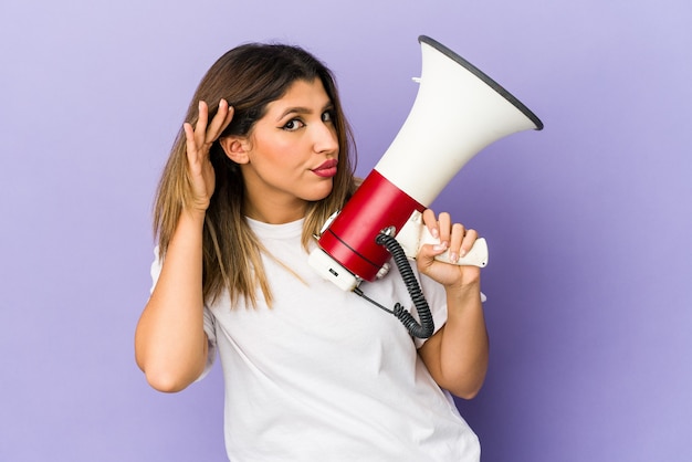 Mujer joven sosteniendo un megáfono aislado tratando de escuchar un chisme