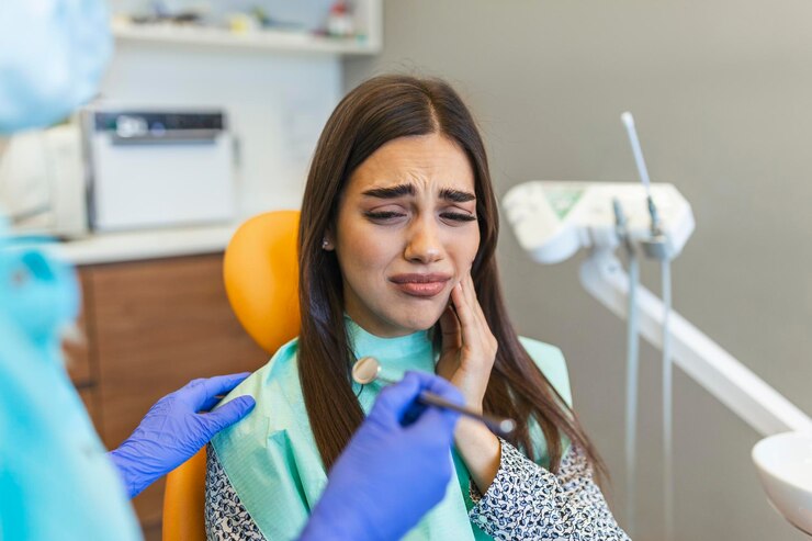 Mujer joven sosteniendo la mejilla en la silla en el dentista que tiene dolor de dientes Fotografía de una mujer joven que sufre de dolor de dientes mientras está sentada en la silla del dentista