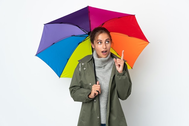 Mujer joven sosteniendo un paraguas aislado en la pared blanca pensando en una idea apuntando con el dedo hacia arriba