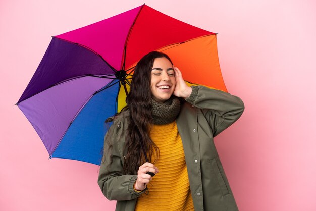 Mujer joven sosteniendo un paraguas aislado sobre fondo rosa sonriendo mucho