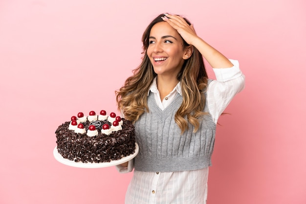 Mujer joven sosteniendo pastel de cumpleaños sobre fondo rosa aislado sonriendo mucho