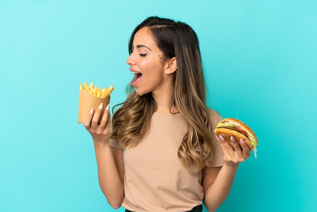 Mujer joven sosteniendo patatas fritas y hamburguesa sobre antecedentes aislados