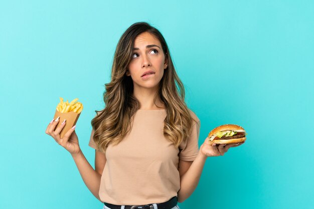 Mujer joven sosteniendo patatas fritas y hamburguesa sobre antecedentes aislados