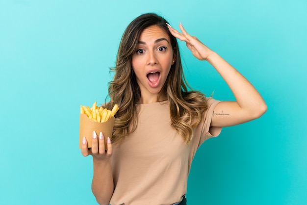 Mujer joven sosteniendo patatas fritas sobre fondo aislado con expresión de sorpresa