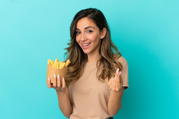 Mujer joven sosteniendo patatas fritas sobre fondo aislado haciendo gesto de dinero