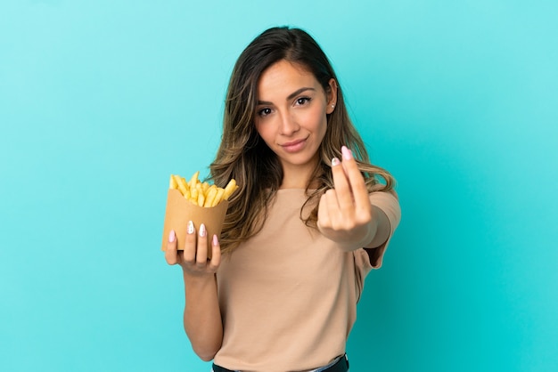 Mujer joven sosteniendo patatas fritas sobre fondo aislado haciendo gesto de dinero
