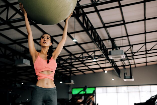 Mujer joven sosteniendo una pelota de fitness mientras hace ejercicio en el gimnasio