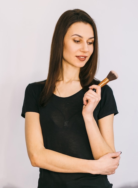 Mujer joven sosteniendo pincel de maquillaje. Posando para la cámara. Fondo blanco.