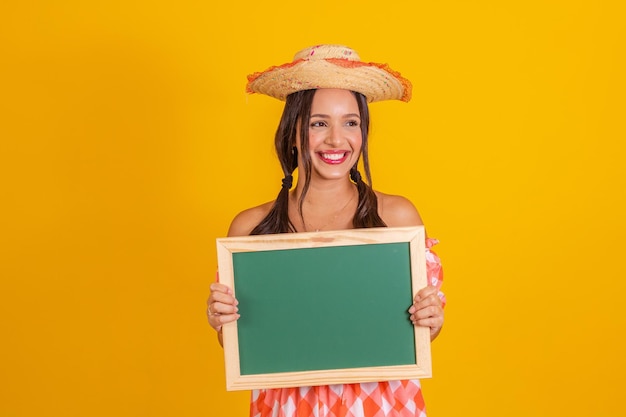 Mujer joven sosteniendo una pizarra con espacio de copia Fiesta de junio Mujer vistiendo ropa de festa junina fiesta típica brasileña