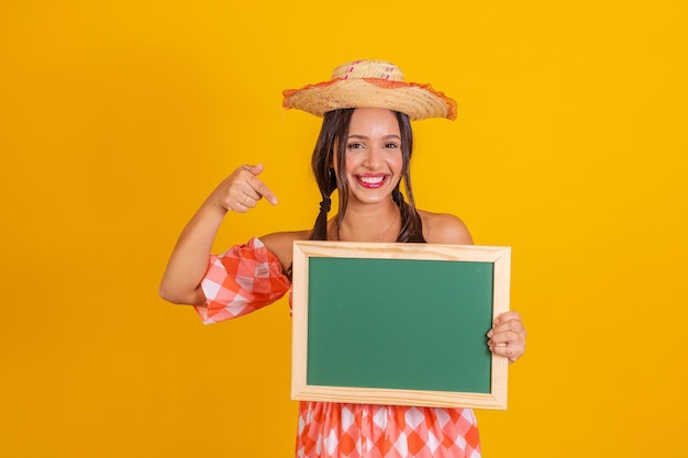 Mujer joven sosteniendo una pizarra con espacio de copia Fiesta de junio Mujer vistiendo ropa de festa junina fiesta típica brasileña