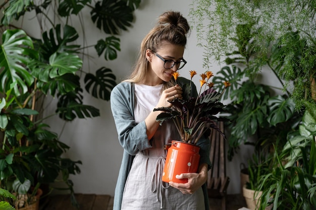 Mujer joven sosteniendo una planta mientras está de pie contra plantas en maceta