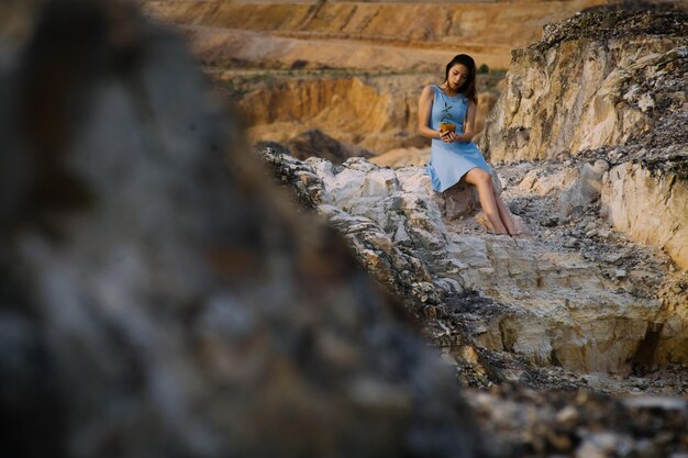 Foto mujer joven sosteniendo una planta mientras está sentada en una roca