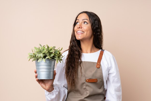 Mujer joven sosteniendo una planta mirando hacia arriba mientras sonríe