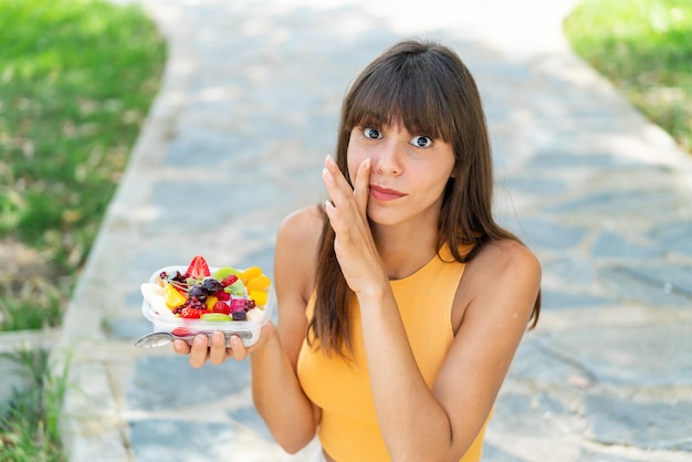 Foto mujer joven sosteniendo un plato de frutas al aire libre susurrando algo