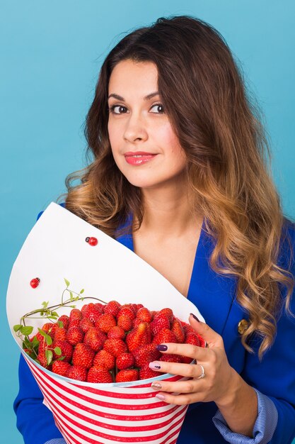 Mujer joven sosteniendo un ramo de fresas sobre fondo azul.