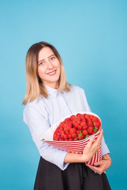 Mujer joven sosteniendo un ramo de fresas sobre fondo azul.