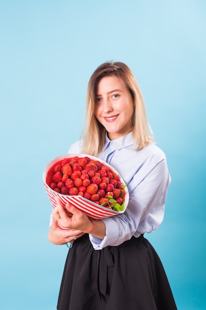 Mujer joven sosteniendo un ramo de fresas sobre fondo azul.