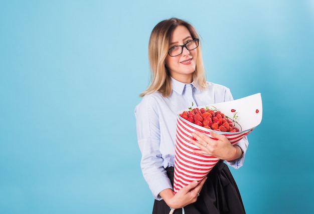 Mujer joven sosteniendo un ramo de fresas sobre fondo azul.