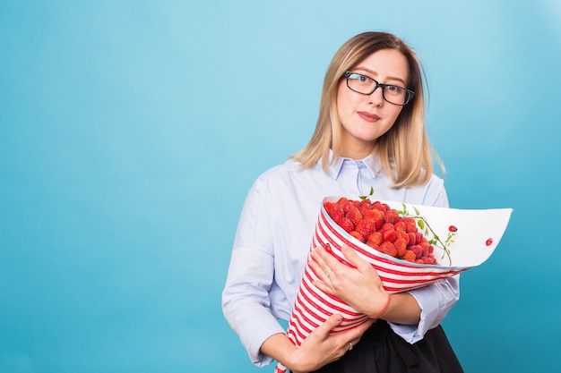 Mujer joven sosteniendo un ramo de fresas sobre fondo azul.