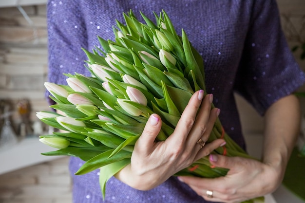 Mujer joven sosteniendo un ramo primaveral de tulipanes rosados blancos en su mano Manojo de flores primaverales recién cortadas en manos femeninasTarjeta de felicitación para el 8 de marzo El concepto de felicitaciones y celebración