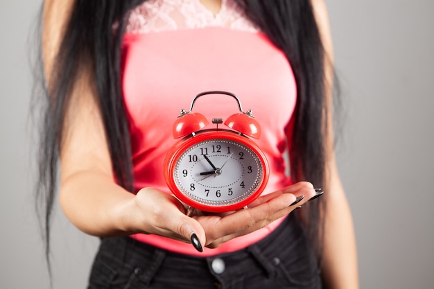 Mujer joven sosteniendo un reloj de alarma sobre fondo gris