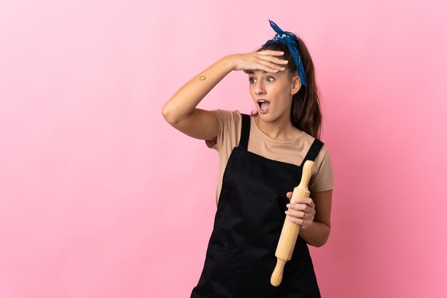 Mujer joven sosteniendo un rodillo haciendo gesto de sorpresa mientras mira hacia el lado