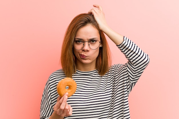 Mujer joven sosteniendo una rosquilla conmocionada, ha recordado una reunión importante.