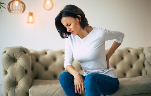 Foto la mujer joven está sosteniendo su espalda baja mientras sufre de dolor de espalda severo.