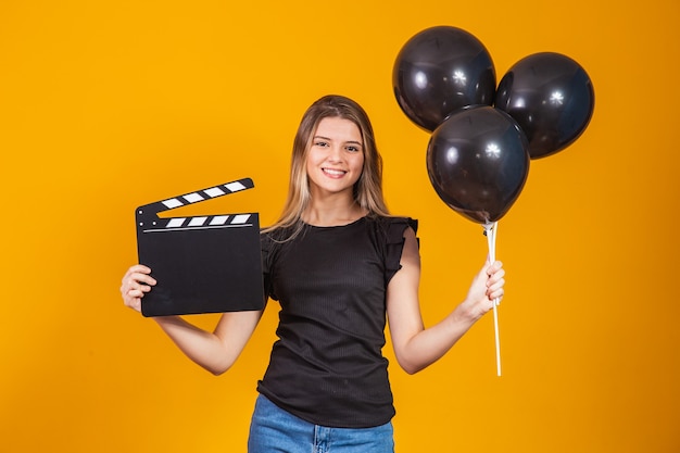 Mujer joven sosteniendo un tablero de chapaleta audiovisual y globos negros durante el Viernes Negro. Concepto de promoción. Viernes negro