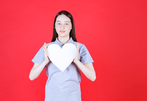 Mujer joven sosteniendo el tablero en forma de corazón y mirando al frente