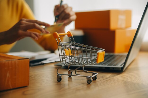 Mujer joven sosteniendo una tableta inteligente que muestra el éxito del pago y la tarjeta de crédito con caja de paquetes amarilla como concepto de compras en línea en la oficina