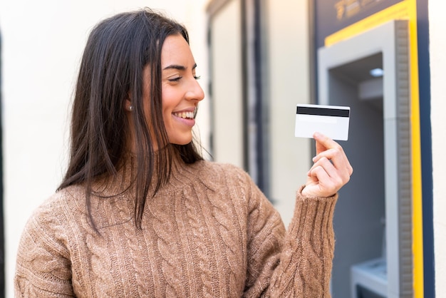 Mujer joven sosteniendo una tarjeta de crédito al aire libre con expresión feliz