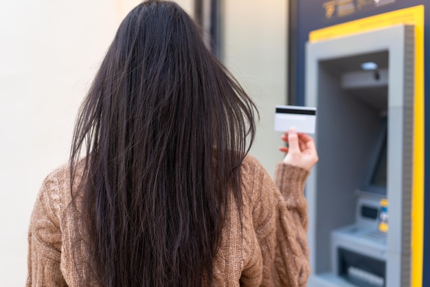 Mujer joven sosteniendo una tarjeta de crédito al aire libre en posición trasera