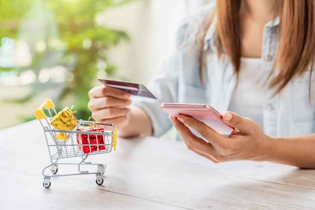 Mujer joven sosteniendo una tarjeta de crédito y usando un teléfono inteligente para realizar compras de pago en línea