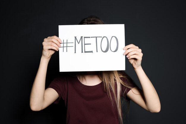 Mujer joven sosteniendo la tarjeta METOO contra un fondo oscuro