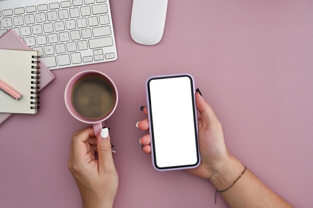 Mujer joven sosteniendo una taza de café y usando un teléfono móvil sobre fondo rosa Vista superior